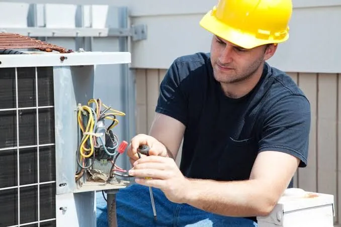 Technician in a hard hat servicing outdoor HVAC wiring